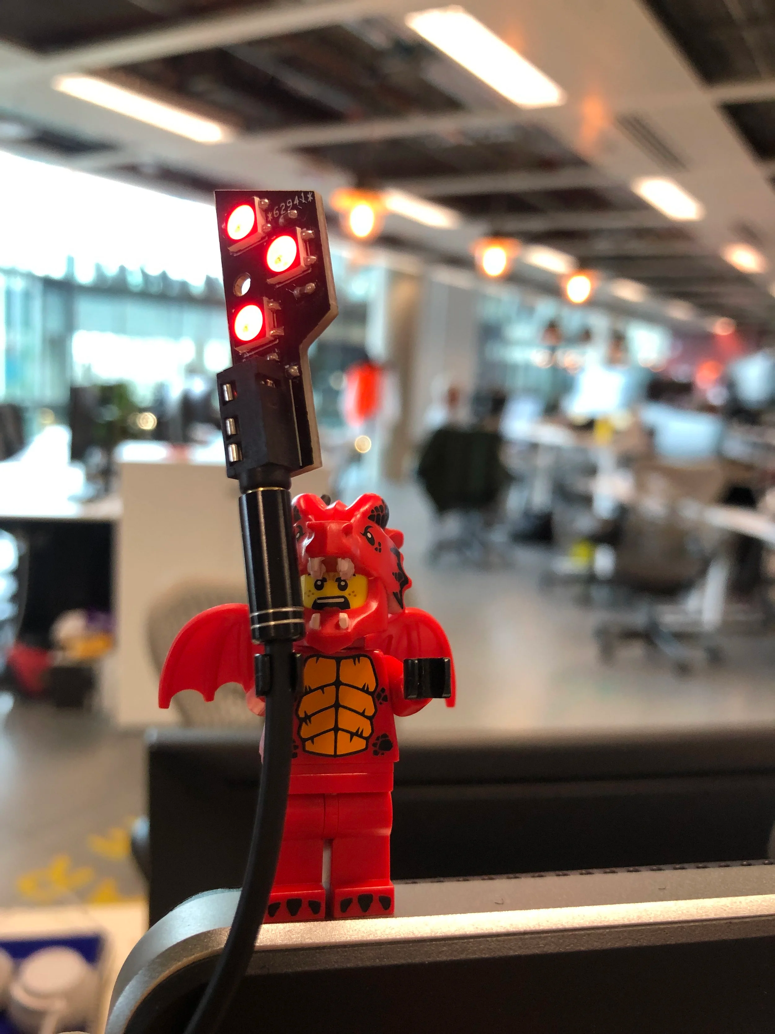 A presence indicator held aloft by a LEGO dragon minifigure on a desk in the D3 Studio open-plan office, LEDs glowing red. Image by Lee Murray.